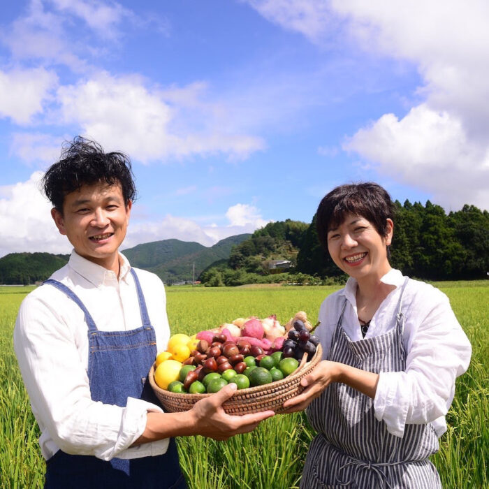 カゴノオトの前と小清水が果物や野菜を持って青空の下で微笑んでいる写真